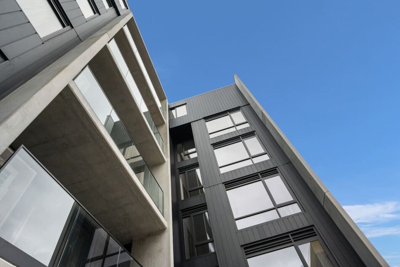 A modern building with a concrete facade, large windows, and a clear sky.