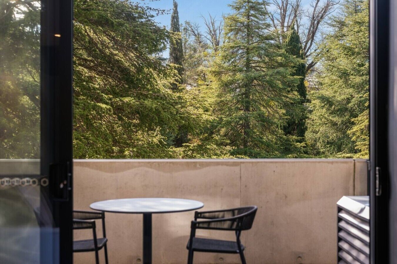 A balcony with a table and chairs, overlooking a forested area.