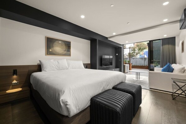A modern hotel room with a large bed, a flat-screen TV, a sofa, and a balcony with a view. - Stylish Canberra Studio with BBQ & Terrace (Braddon)