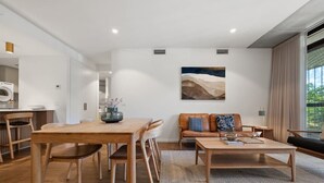 A modern living room with a wooden dining table, a sofa, and a coffee table. - 2BR Haig Park View w/ Balcony & Secure Car Space! (Braddon)