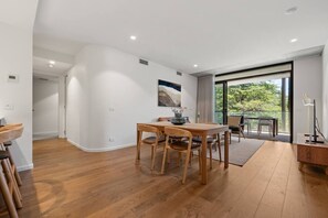 Ein geräumiges Zimmer mit einem Holzesstisch, Stühlen und einem großen Fenster mit Blick auf Grünflächen.