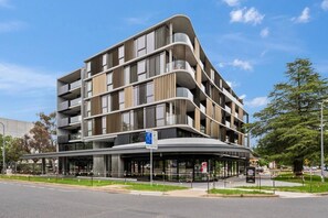 A multi-story building with a curved facade, balconies, and a covered entrance area. - Amazing Studio Apartment w/ Balcony & Parking! (Braddon)