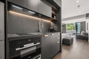 A modern kitchen with a built-in oven, microwave, and sink. There is a seating area with a view of the outdoors. - Amazing Studio Apartment w/ Balcony & Parking! (Braddon)