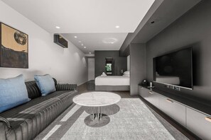 A modern hotel room with a sofa, a bed, a TV, and a large window. - Amazing Studio Apartment w/ Balcony & Parking! (Braddon)