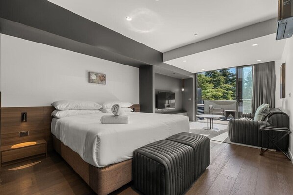 A modern hotel room with a large bed, a flat-screen TV, a seating area with a view, and a balcony. - Amazing Studio Apartment w/ Balcony & Parking! (Braddon)
