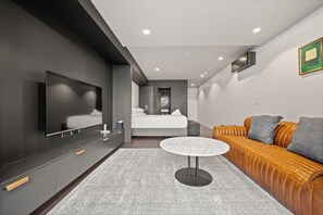 Ein modernes Hotelzimmer mit großem Flachbildfernseher, einer Couch, einem runden Couchtisch und einem Bett mit Blick.
