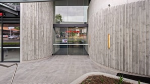 Une entrée moderne avec des portes en verre, un mur en béton et une rambarde en métal.