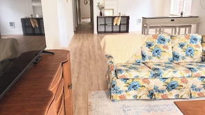 A living room with a TV, wooden furniture, a floral sofa, and a hallway leading to a dining area. - 2-bedroom/2bath condo near downtown Spokane (Spokane)