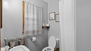 Een badkamer met toilet, wastafel, handdoekhouder en een raam met gordijnen.