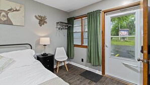 Een motelkamer met een bed, een stoel, een lamp, een kapstok en een deur met uitzicht op het motelbord.