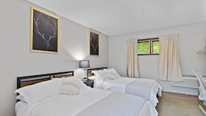 Ein Hotelzimmer mit zwei Betten, einem Nachttisch, einer Lampe, einem Fenster mit Vorhängen und Bildern an den Wänden.