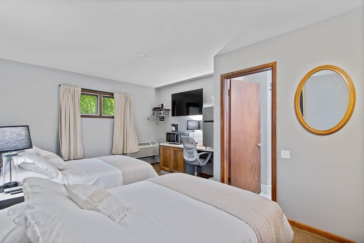 A hotel room with two beds, a desk with a computer, a television, and a window with curtains.