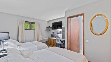 A hotel room with two beds, a desk with a computer, a television, and a window with curtains.