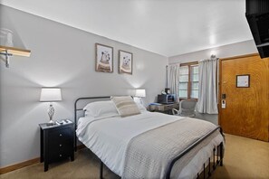 A bedroom with a bed, bedside tables, a desk with a chair, a window with curtains, and two framed pictures on the wall. - Room 5, Kozy Rest Motel (Montello)