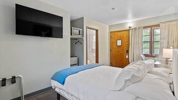 A bedroom with a bed, a TV mounted on the wall, a microwave, and a door leading to another room.