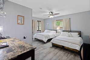 A room with two beds, a desk, a ceiling fan, and a window with curtains.