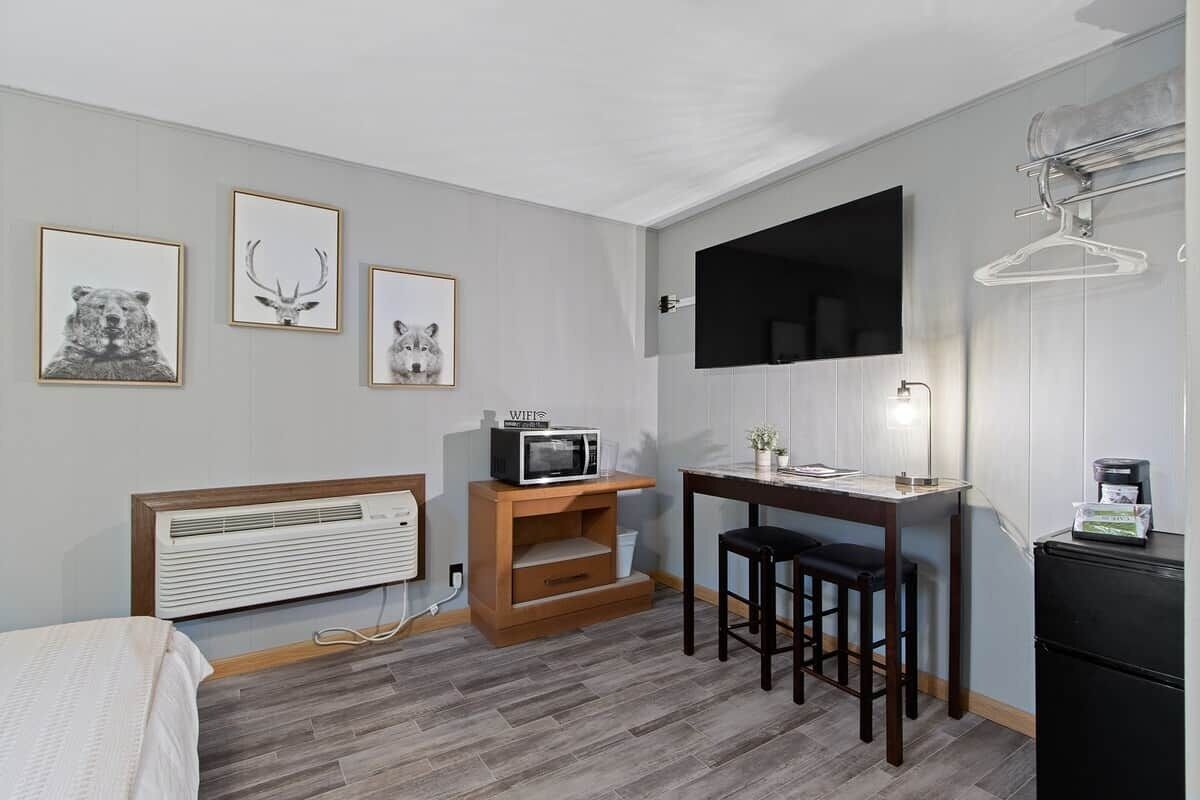 Une chambre compacte comprenant un lit, un petit bureau avec une chaise, un four à micro-ondes et un téléviseur fixé au mur.
