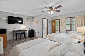 Une chambre d’hôtel avec deux lits, un bureau avec une télévision, un ventilateur de plafond et une vue sur l’extérieur.