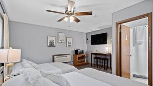 Een hotelkamer met twee bedden, een plafondventilator, een bureau met stoel, een televisie en een douche.