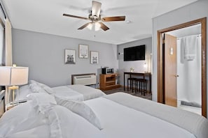 Ein Hotelzimmer mit zwei Betten, einem Deckenventilator, einem Schreibtisch mit Stuhl, einem Fernseher und einer Dusche.