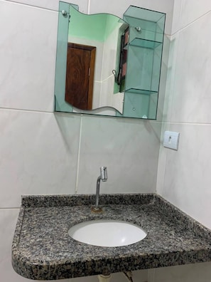 Une salle de bain avec un lavabo surmonté d’un plan de travail en granit, un miroir en verre et une porte en bois.