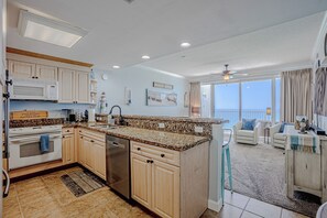 A modern kitchen with granite countertops, wooden cabinets, a built-in oven, and a dishwasher. - Boardwalk Breeze; cozy 2 bedroom with amazing view (Panama City Beach)