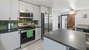 A modern kitchen with stainless steel appliances, a microwave, oven, and refrigerator. There is a dining area with a wooden table and benches.