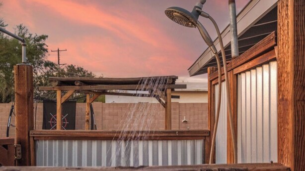 A wooden deck with a showerhead, a target board, and a corrugated metal wall.