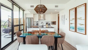 A modern kitchen with white cabinets, a hanging light fixture, and a dining area with a glass table and chairs.