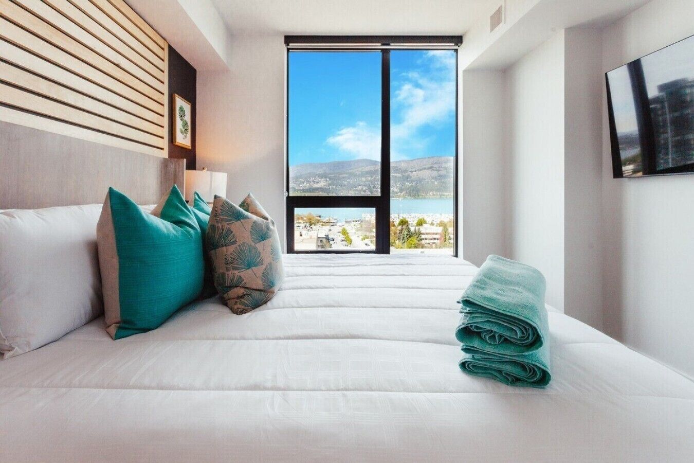 Habitación de hotel con cama, almohadas, vistas a un cuerpo de agua y un ventanal grande.