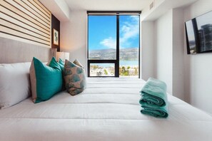 A hotel room with a bed, pillows, a view of a body of water, and a large window.
