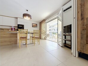 A modern kitchen with wooden cabinets, a dining area with two chairs, a pendant light, and a view of the outside. - L'Instant Azur, Beach, on foot, Clim Garage (Fréjus)