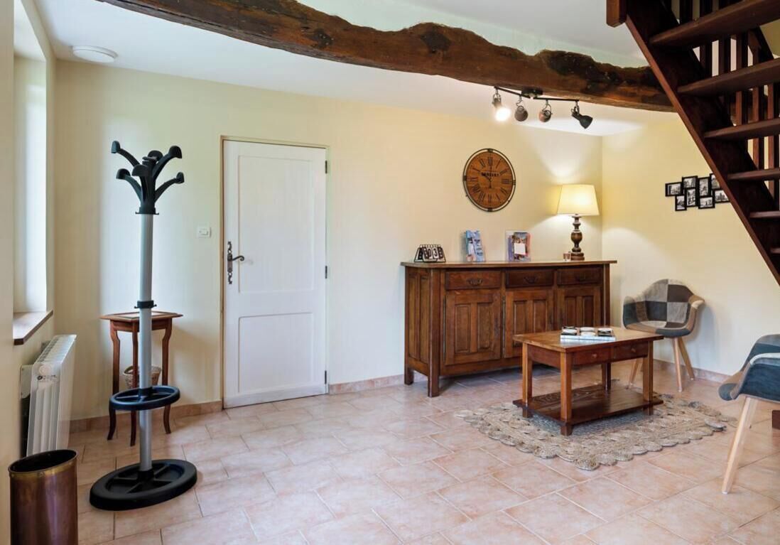 Un salon avec une table en bois, une lampe, un porte-manteau, une porte et un escalier.