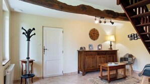 A living room with a wooden table, a lamp, a coat rack, a door, and a staircase. - Gîtes de France® - The Little House on the Prairie (ANCRETTEVILLE SUR MER)