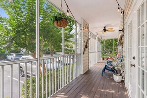 Une véranda couverte avec un plancher en bois, des rampes blanches, des plantes suspendues et un ventilateur de plafond.