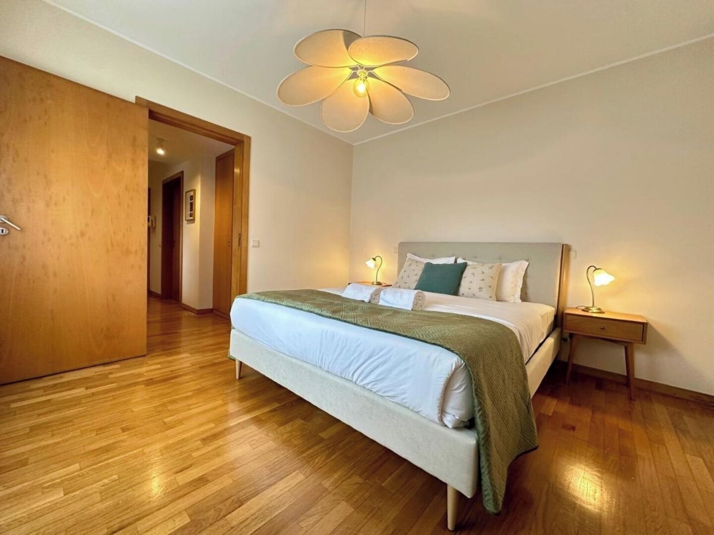 Quarto com cama, luminárias de cabeceira, porta de madeira e ventilador de teto.
