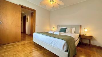 Quarto com cama, luminárias de cabeceira, porta de madeira e ventilador de teto.