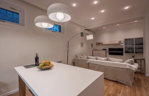 Ein modernes Wohnzimmer mit einem weißen Sofa, einem Esstisch mit Obstschale und Einbau-Deckenleuchten.