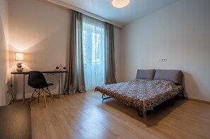 Een slaapkamer met een bed, een bureau, een stoel en een raam met gordijnen.