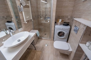 Een moderne badkamer met een wastafel, toilet, wasmachine en douchecabine.