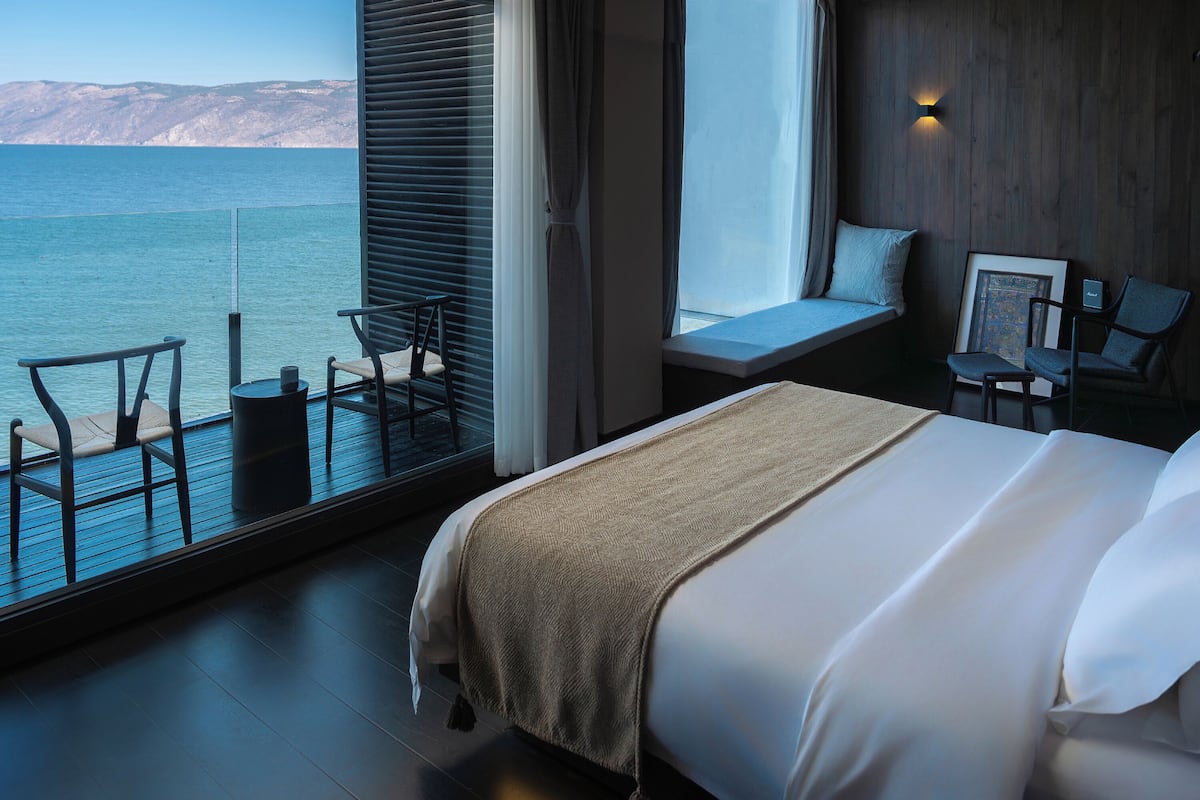 A bedroom with a large window, a bed, a chair, and a small table.
