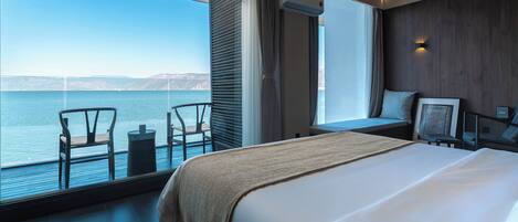 Habitación de hotel con una cama grande, vista al mar, zona de estar con sillas y una pared de madera.