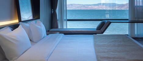 A hotel room with a bed, a window with a view of the sea and a bridge, and a framed picture on the wall.