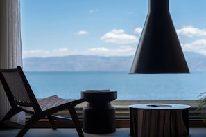 A chair and a table by a window with a view of the sea and mountains.