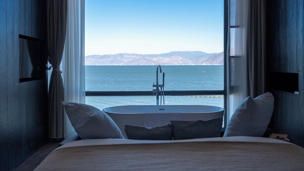 A bedroom with a large window, a round bathtub, and a bed with pillows. - Anye Seaview Hotel Dali (Dali)