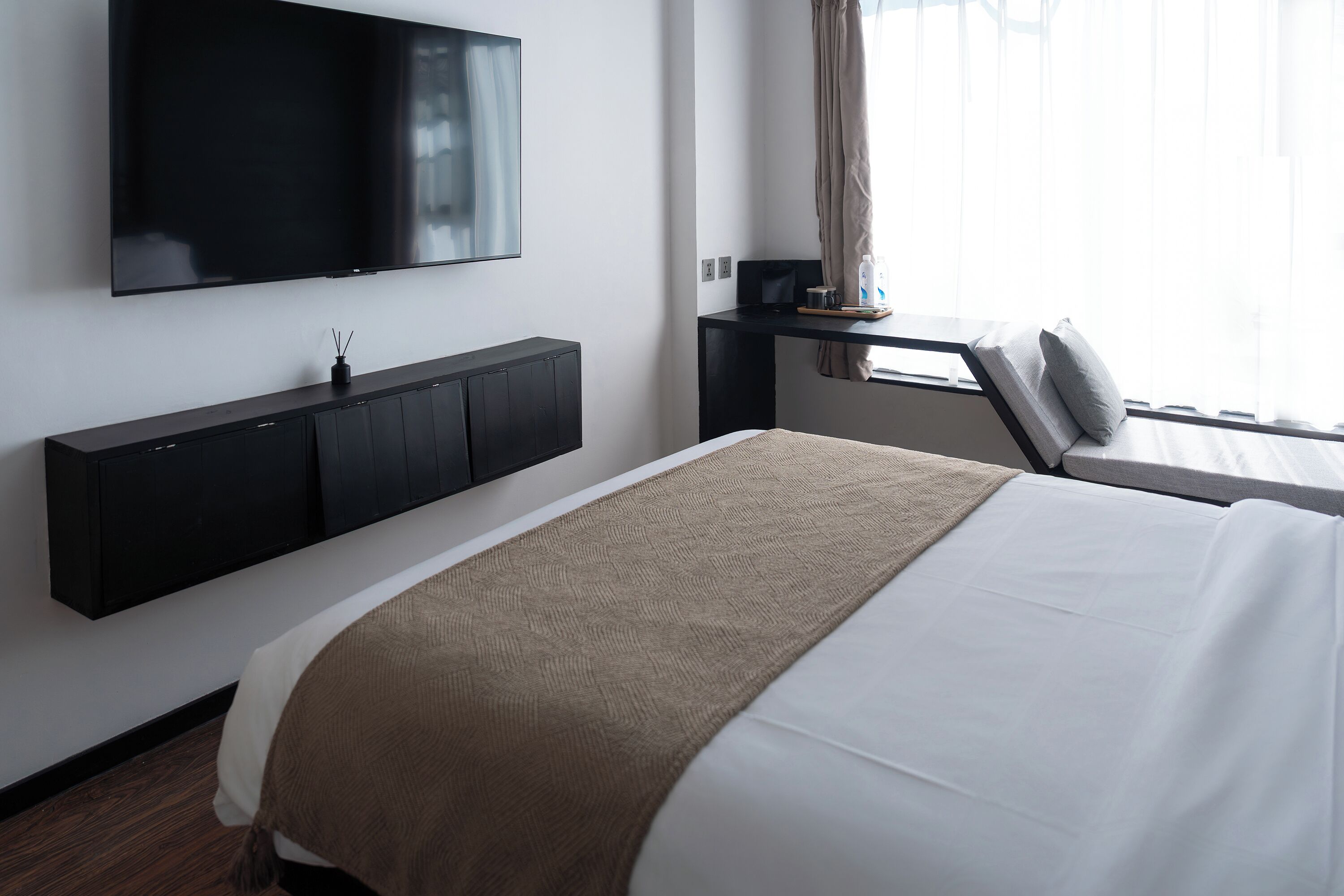 Ein modernes Hotelzimmer mit einem großen Bett, einem Flachbildfernseher an der Wand, einem Schreibtisch mit Computer und einem Vorhangfenster.