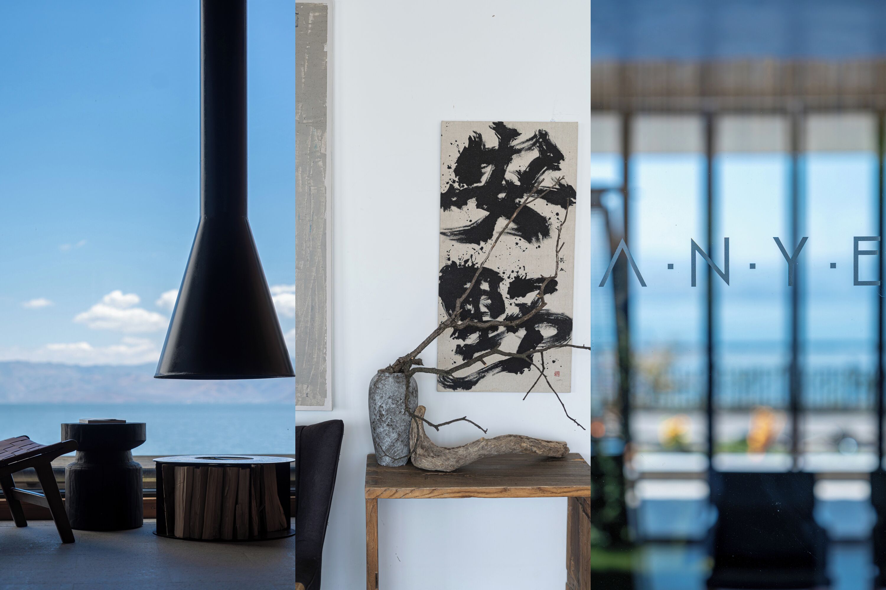 Un interior moderno con vista al mar, una lámpara negra, una mesa de madera y una obra de arte abstracta.