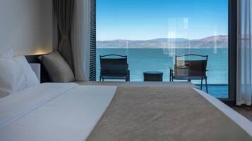 A hotel room with a large bed, two chairs, a small table, and a view of the water.