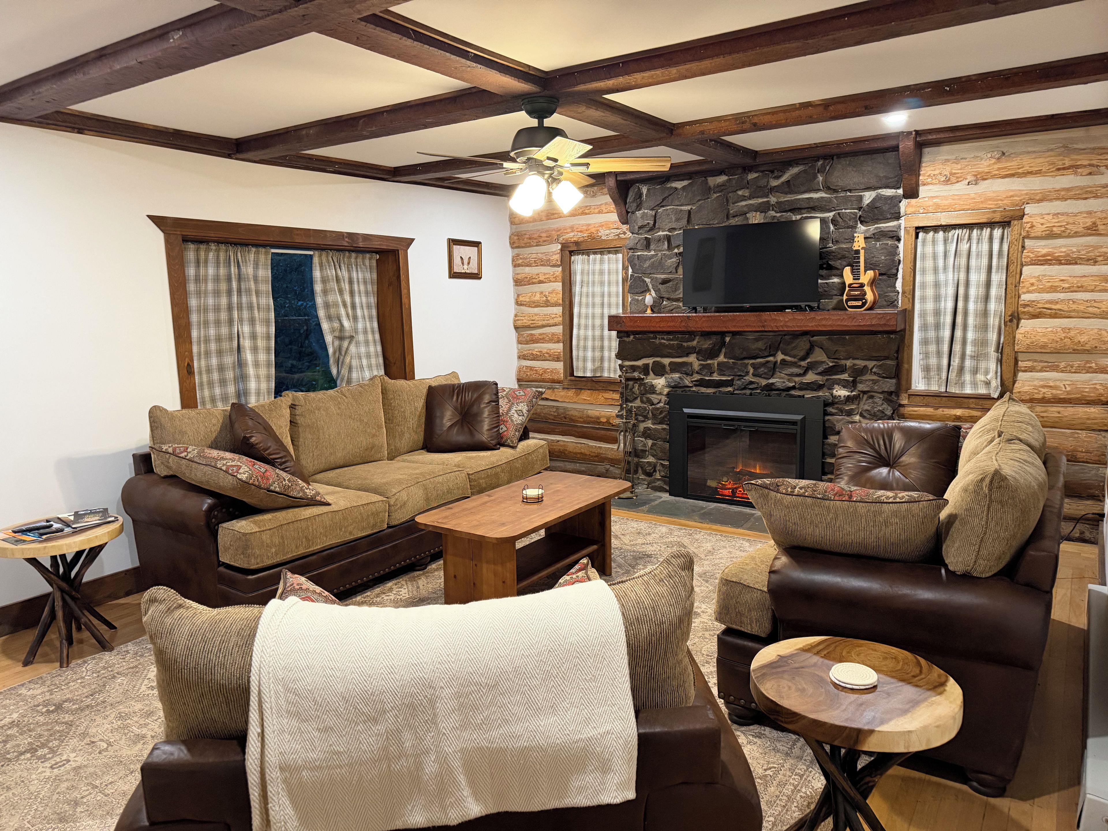 A cozy living room with a stone fireplace, wooden beams, and a television.