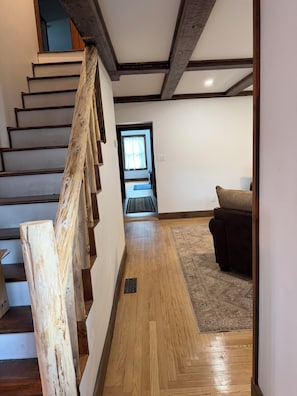 A staircase with wooden steps and a handrail, leading to a room with a patterned rug and a brown sofa.